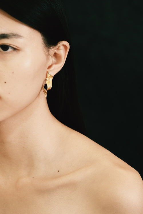 Close-up of a person wearing gold earrings with a black background