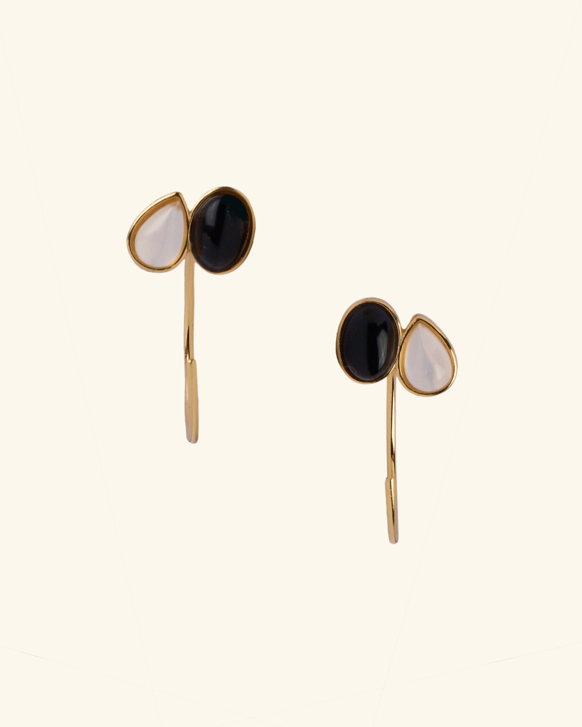 Pair of earrings with gold, black, and white stones on a beige background