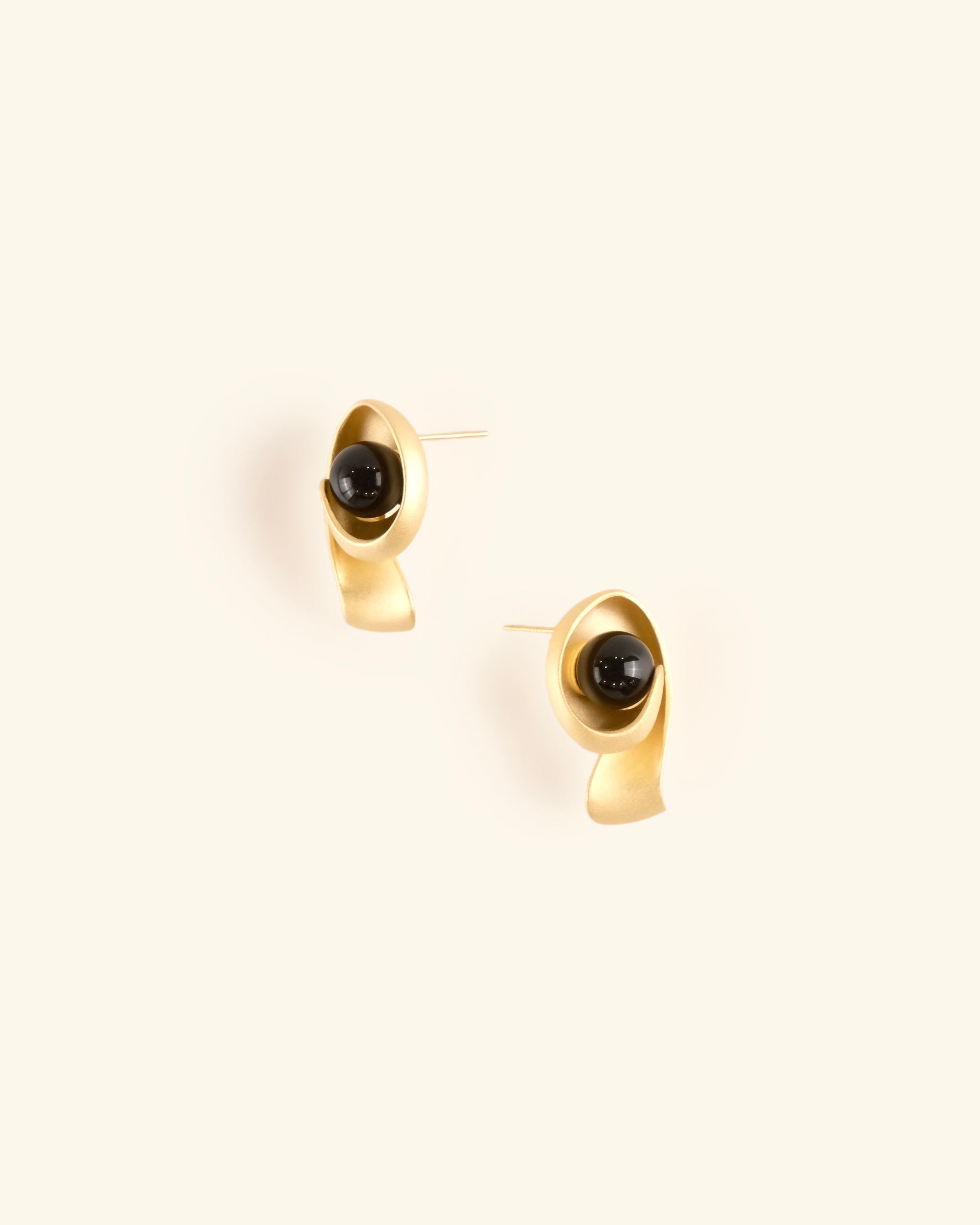 Gold earrings with black stones on a light beige background