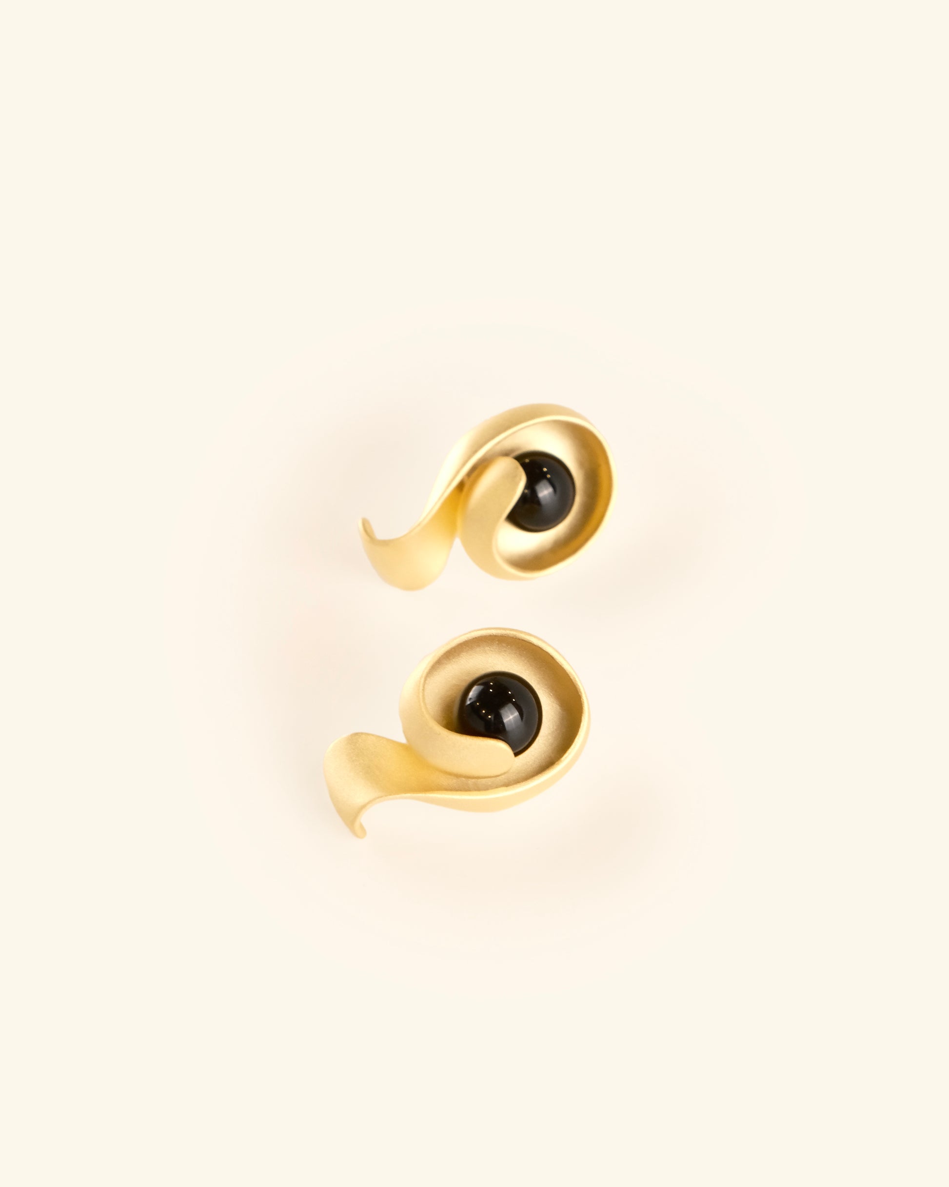 Pair of gold earrings with black gemstones on a beige background