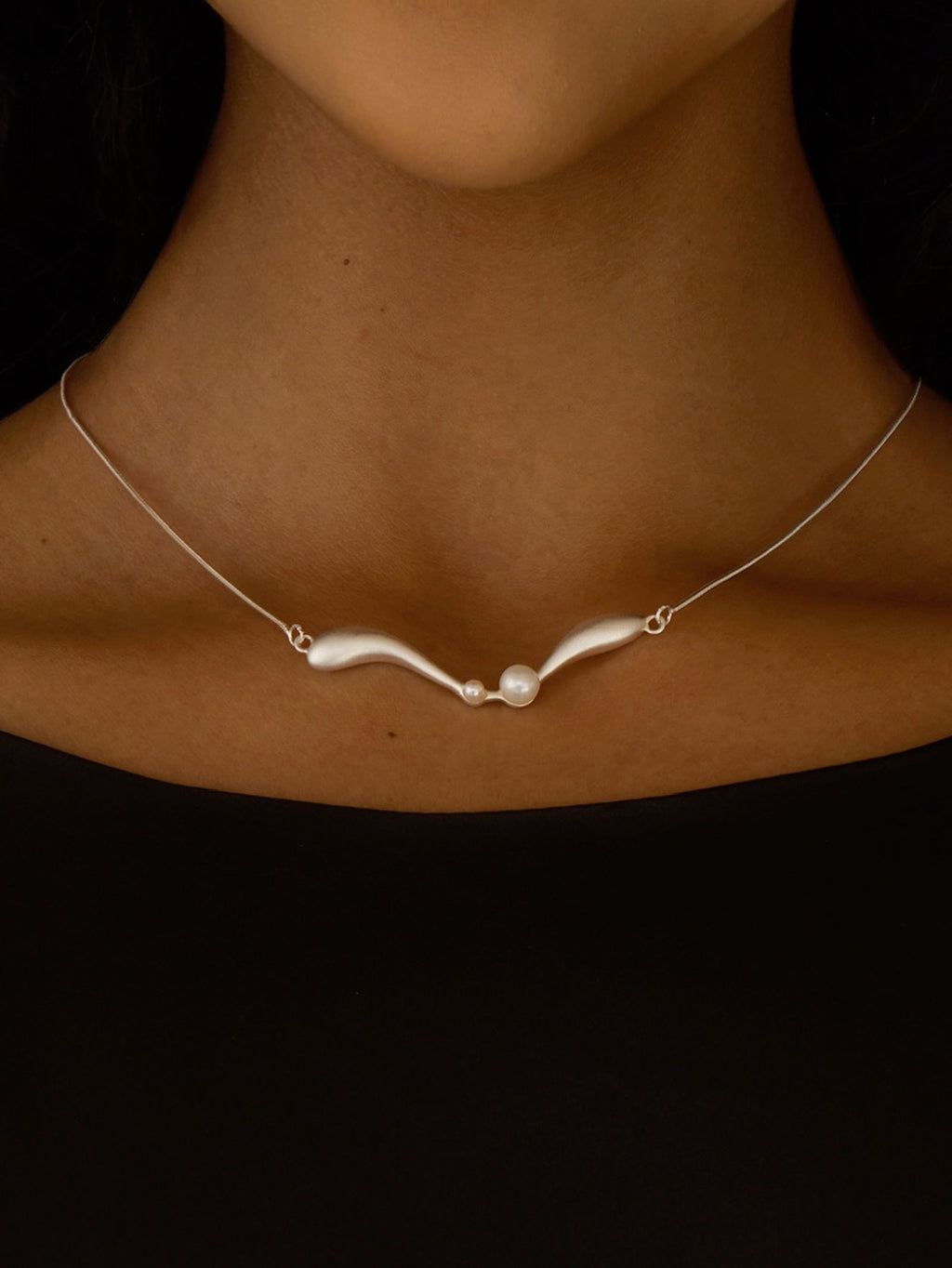 Necklace with a pearl pendant on a person's neck against a black background