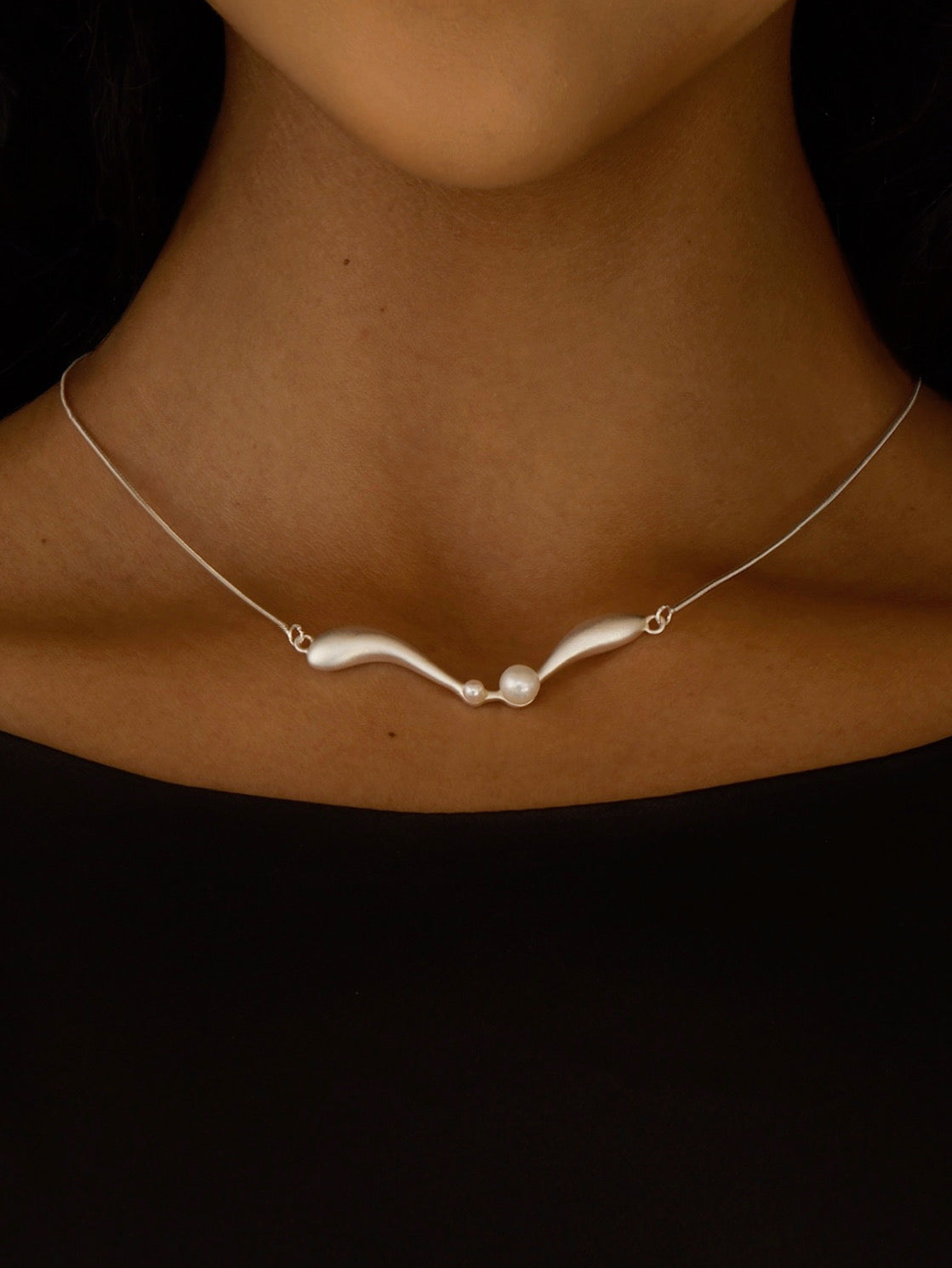 Necklace with a pearl pendant on a person's neck against a black background